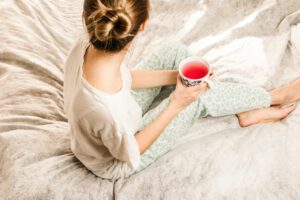 Frau sitzt mit Teetasse im Bett