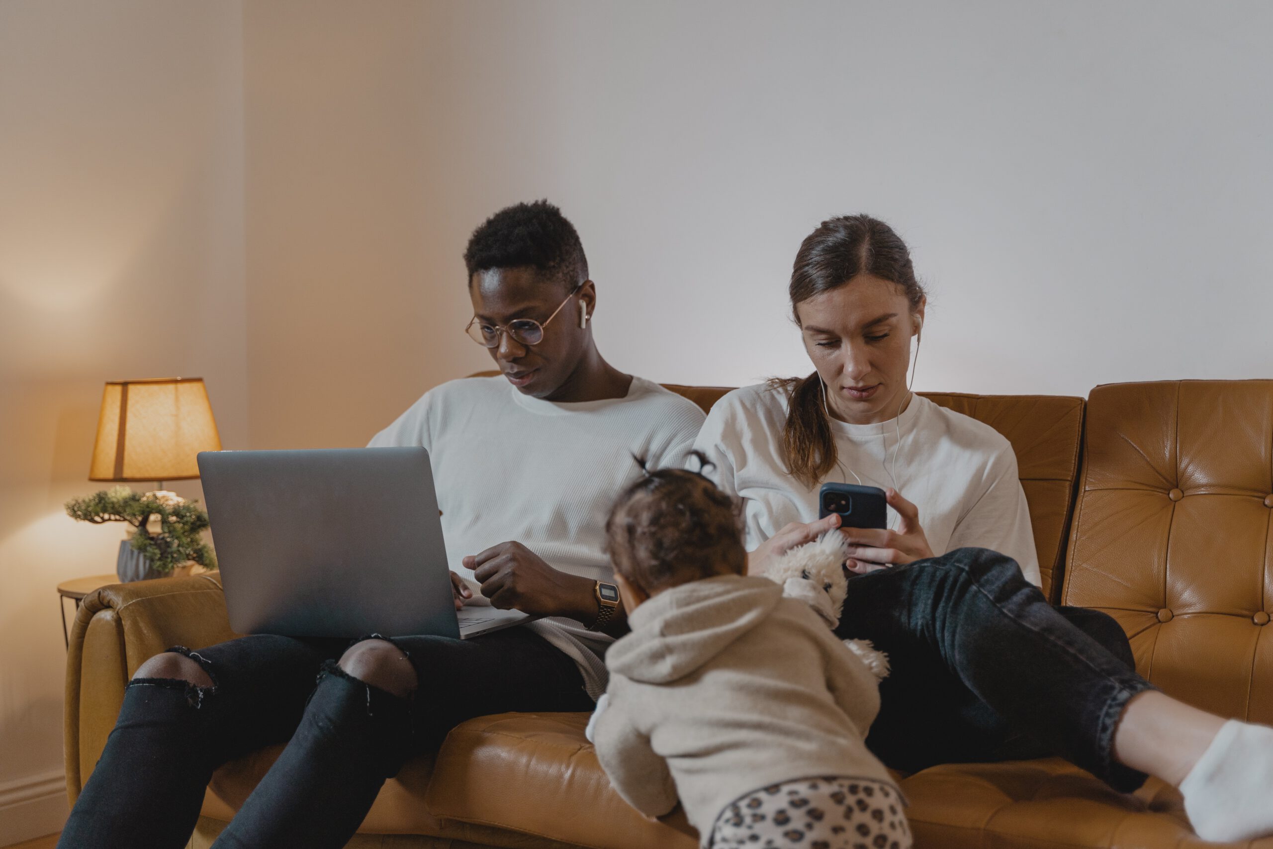 Paar sitzt mit Kind auf Couch und schaut aufs Smart Phone